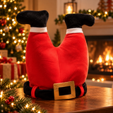 Santa Legs plush on a wooden table in front of a Christmas tree and fireplace